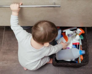 Toddler reaching for cleaning products underneath a bathroom cabinet - pediatric poisoning concept