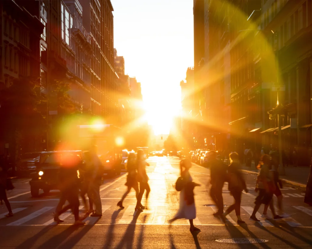 People walking across city street with sun setting in background