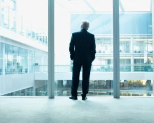 older businessman looking out glass wall of office