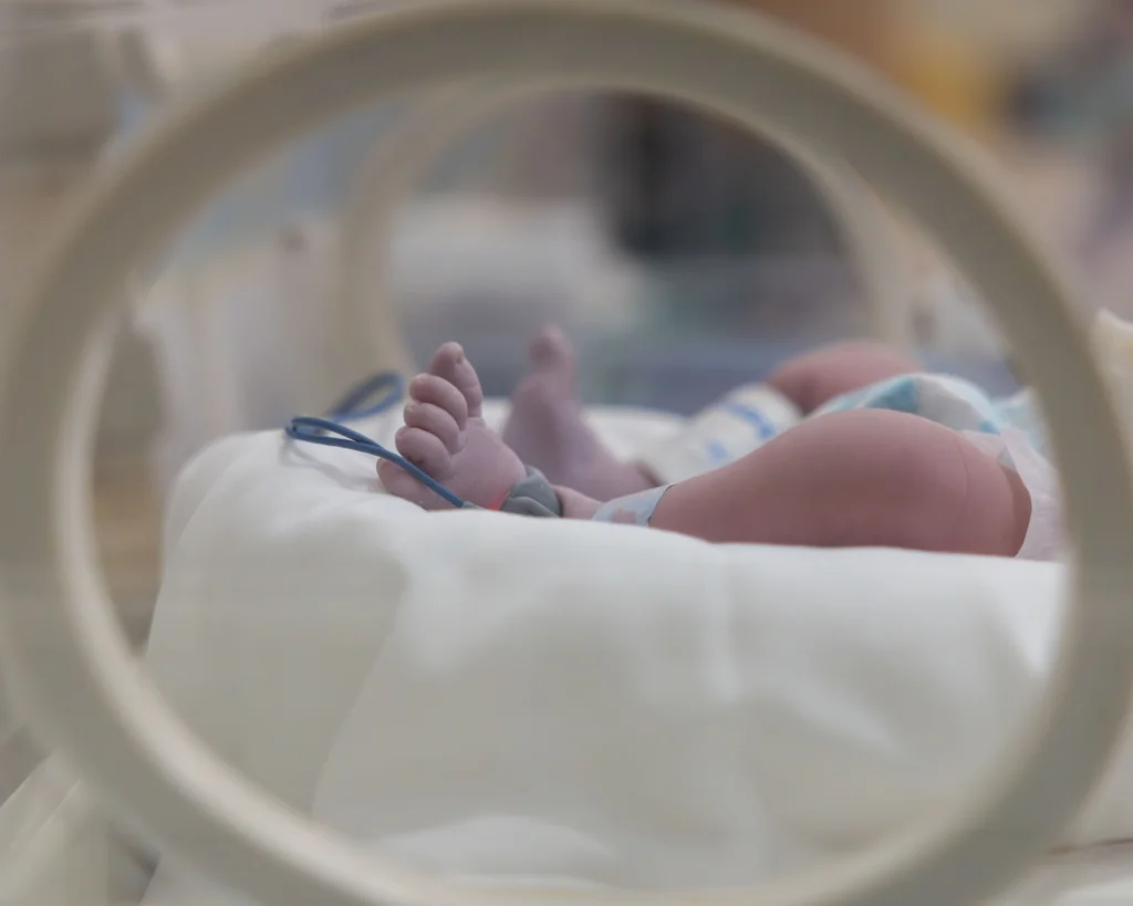 A newborn baby's feet are visible in a hospital incubator. Neonatal health concept