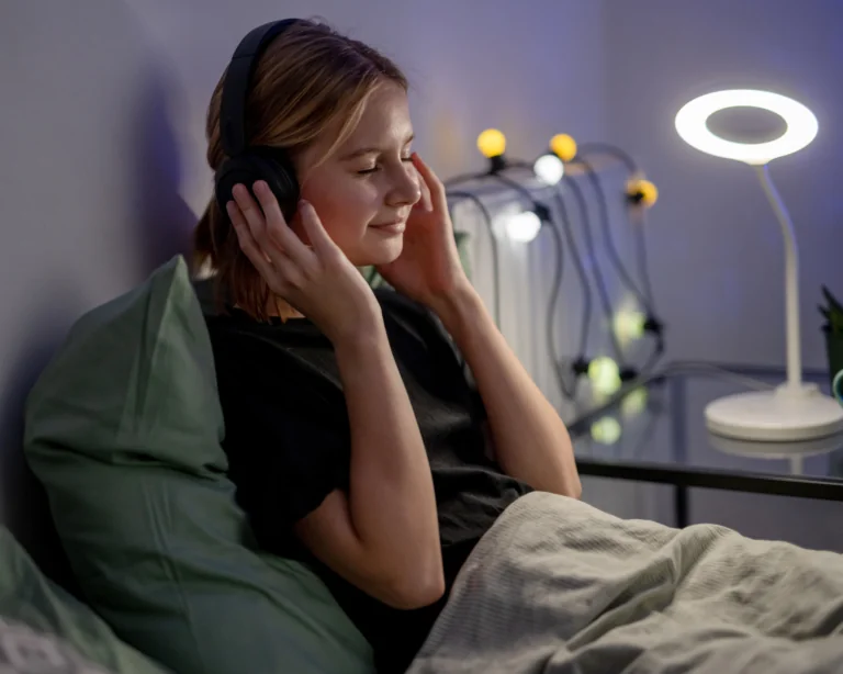 Young woman sitting in bed listening to music through headphones