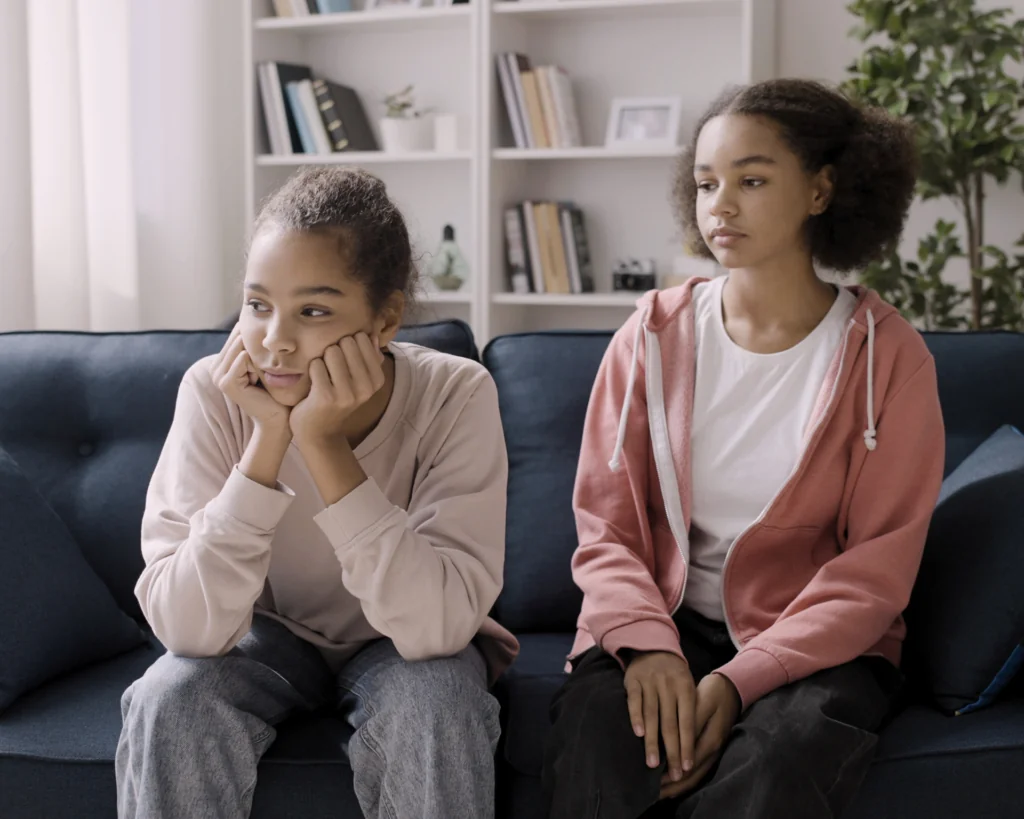 Portrait of two young, sad women sitting on a couch. Sibling trauma concept