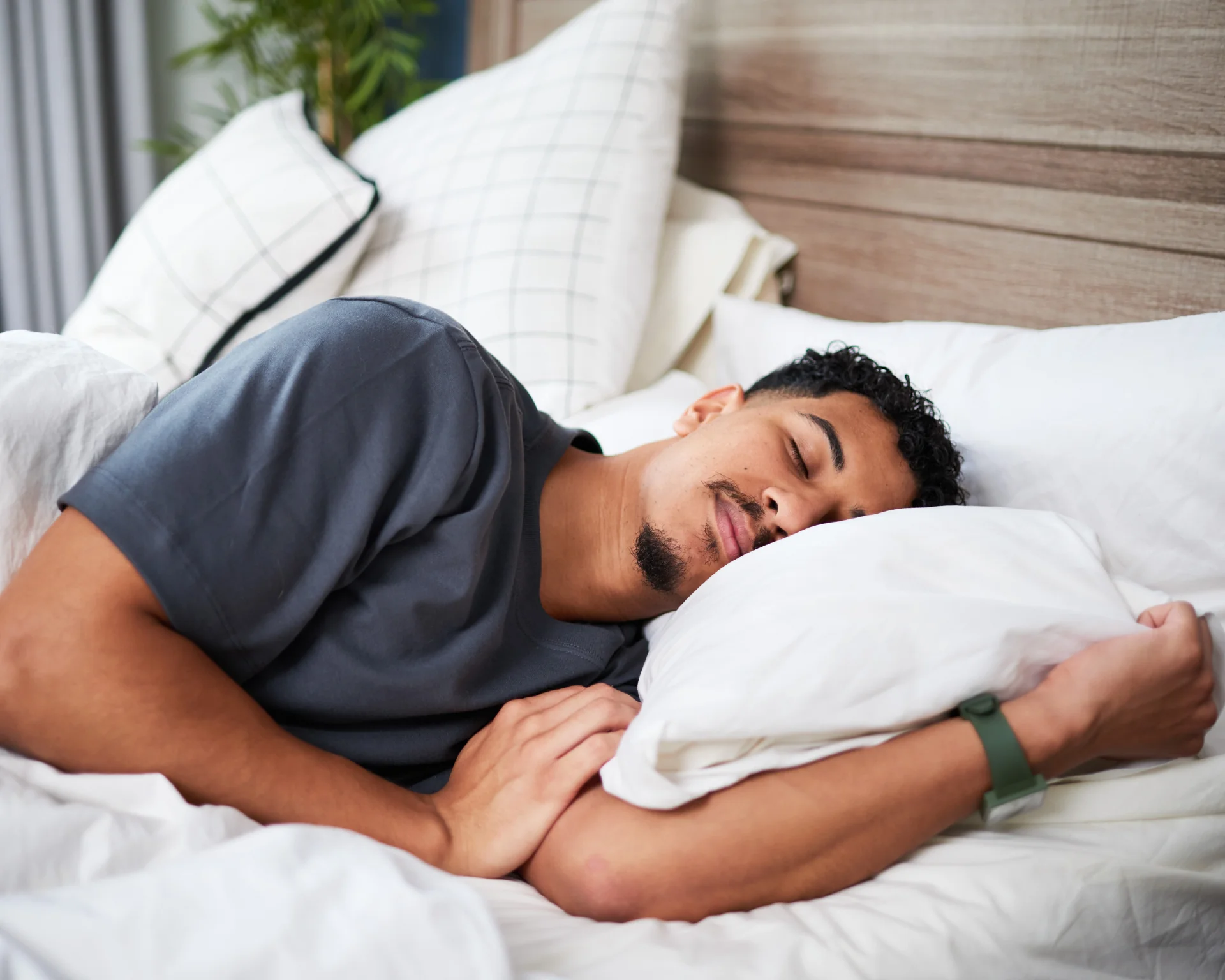 portrait of a young man is sleeping soundly on a cozy bed, embracing a pillow while surrounded by soft white linens, captured in a serene and calm moment within a home setting.