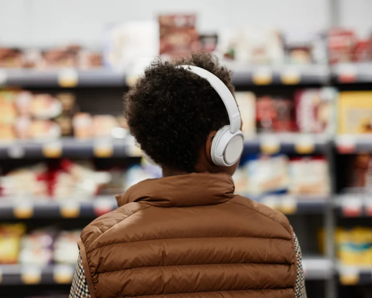Back view of a teenage boy wearing headphones and looking at food items on a grocery store shelf
