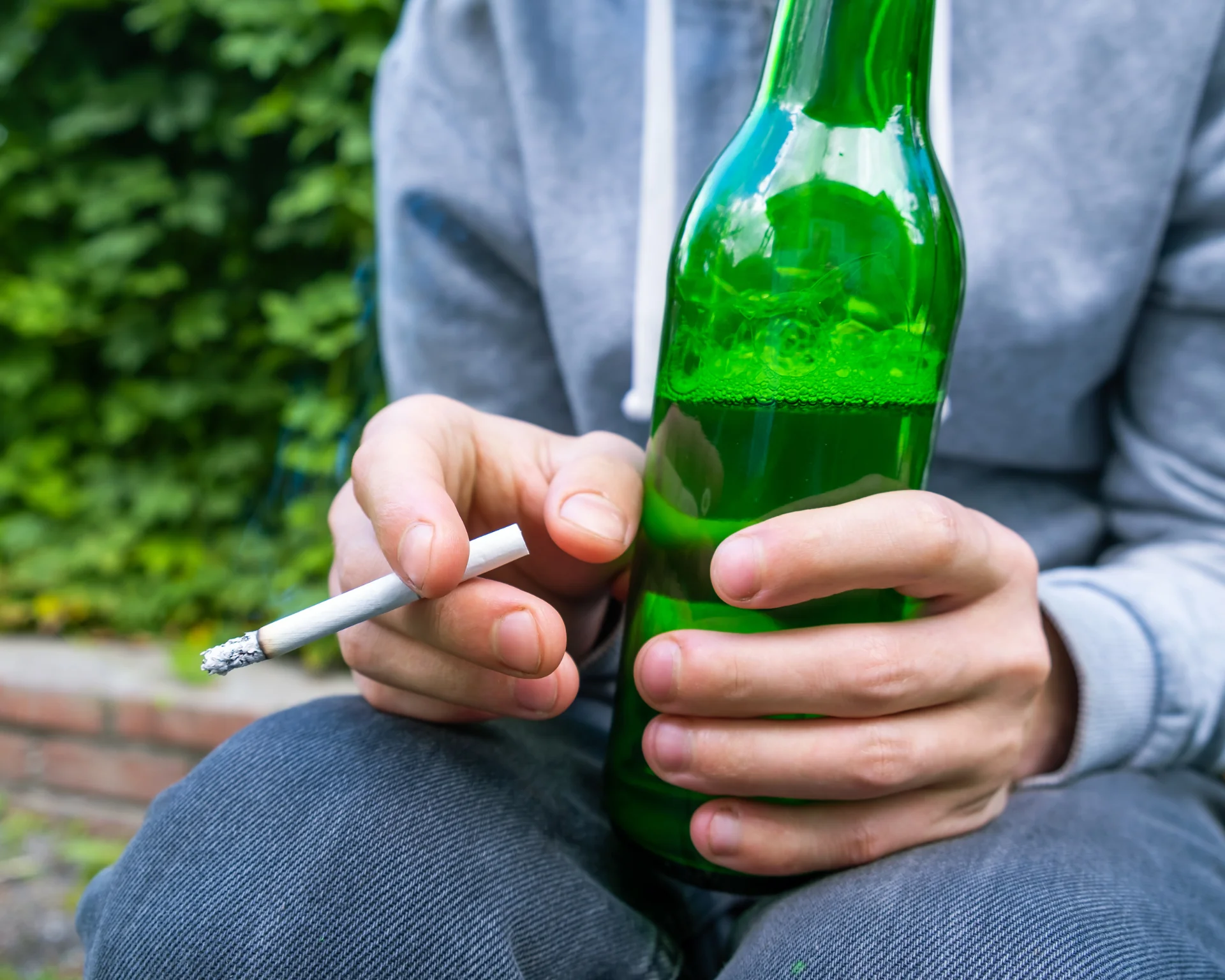 Close-up portrait of a young person holding a beer and smoking a cigarette. Teen substance use concept