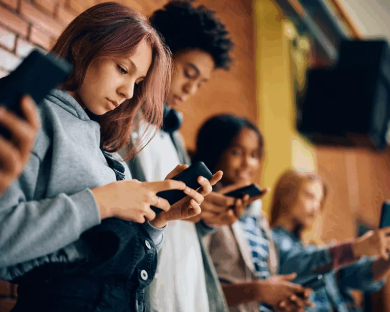 Group of adolescents using mobile phones in hallway at high school