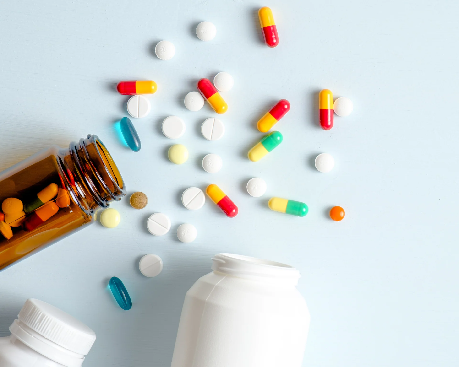 Medical drug bottles and medication pills spilling out onto a pastel blue background. Top view with copy space. Healthcare, pharmacy, medicine concept