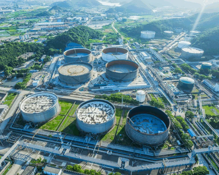Large crude oil storage tanks beneath an oil refinery in a green hilly area