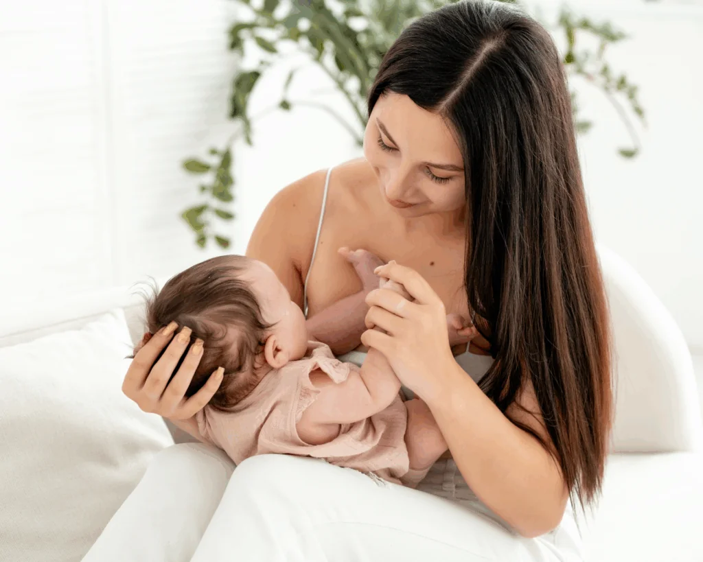 A young mother holds a small newborn baby in her arms, gently hugging and kissing him at home in a bright room
