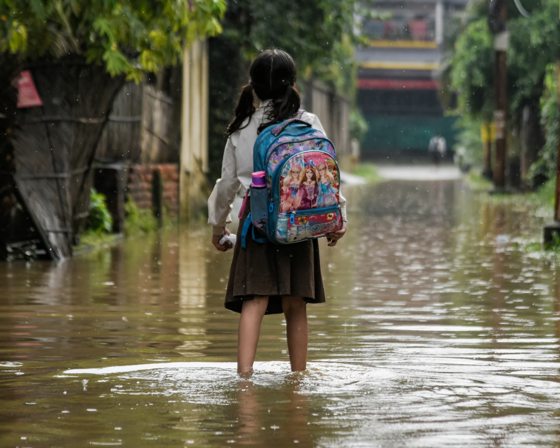 A girl returns from school wades across a flooded street after heavy rains. Indicates connection between climate change and child health