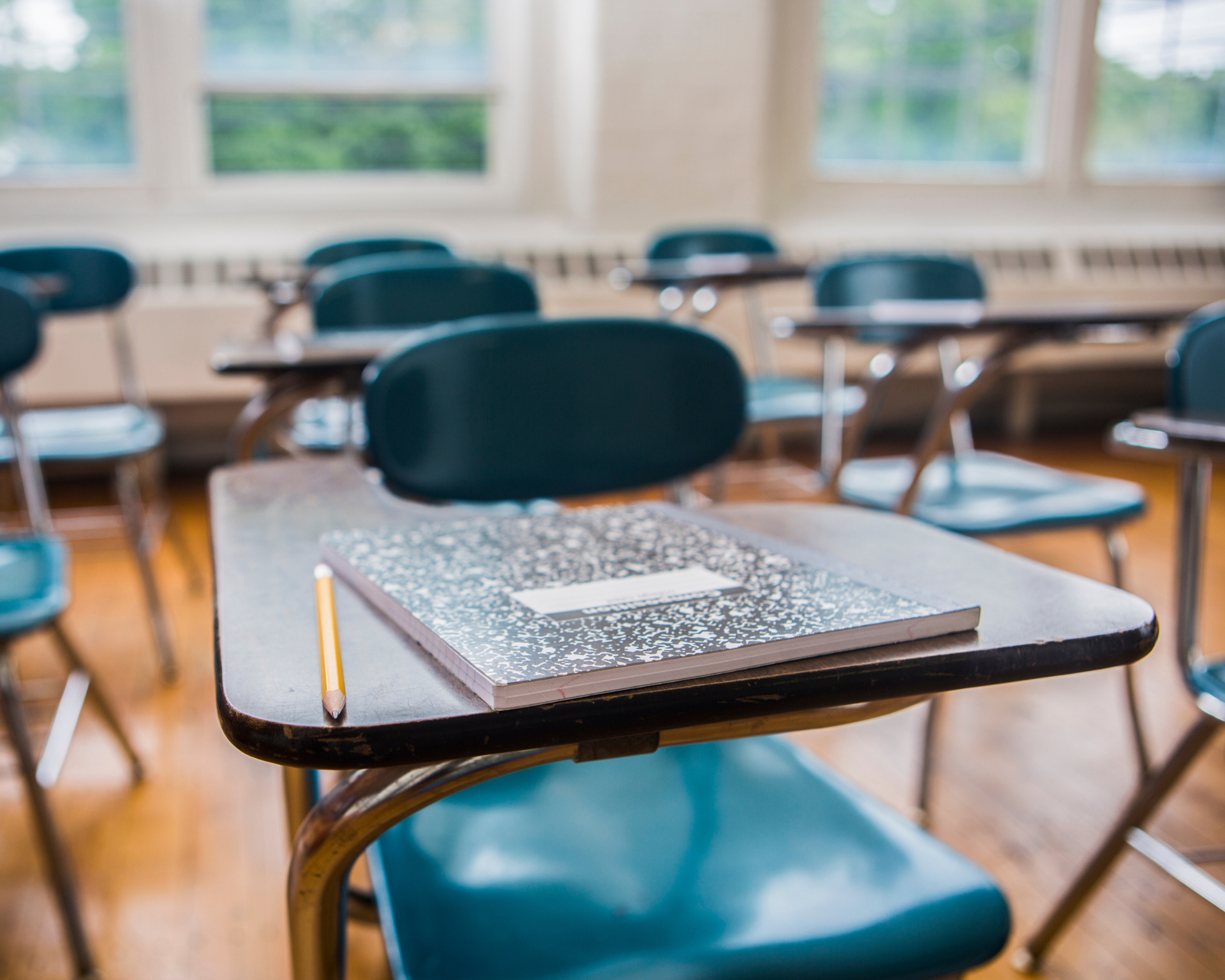 A notebook and pencil on a desk in a school classroom