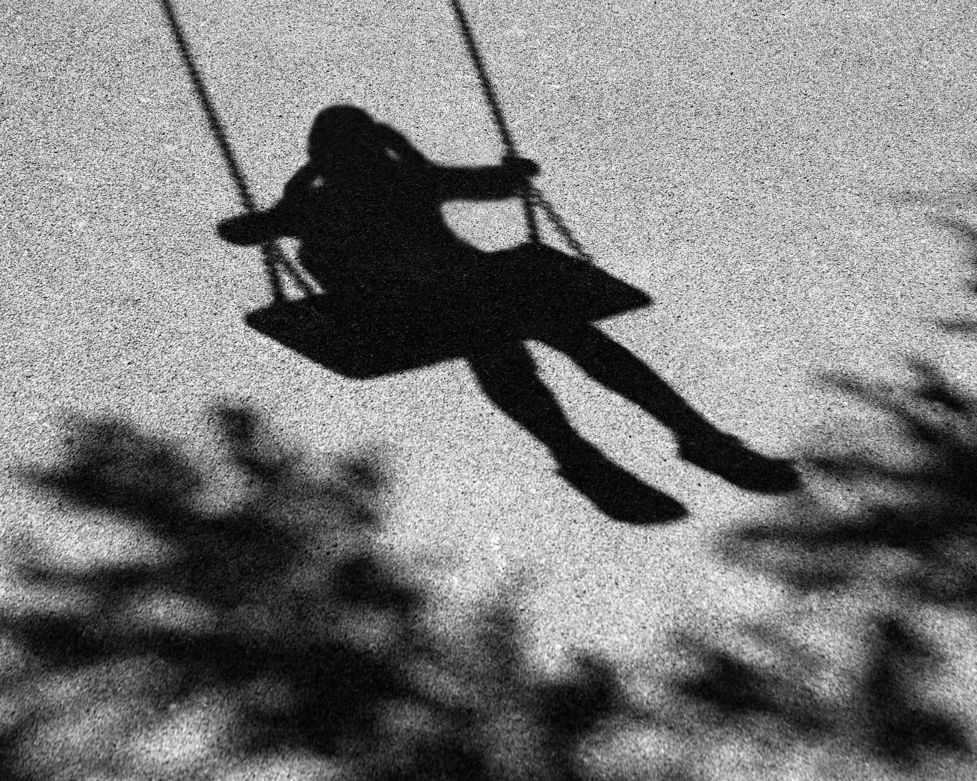 Blurry, black and white shadow of a girl swinging on a swing that is attached to a tree branch
