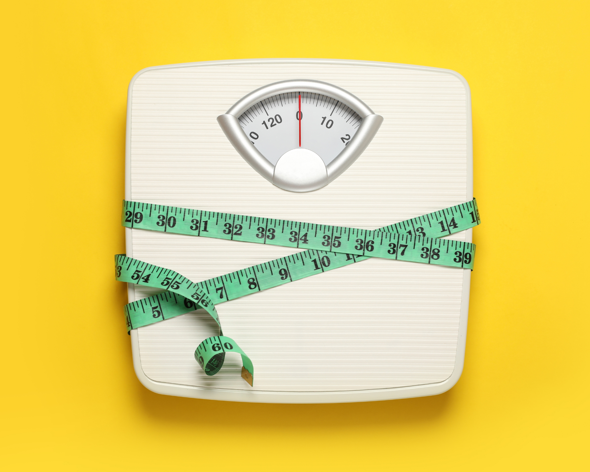 Weigh scales tied with measuring tape on a yellow background, top view. BMI concept