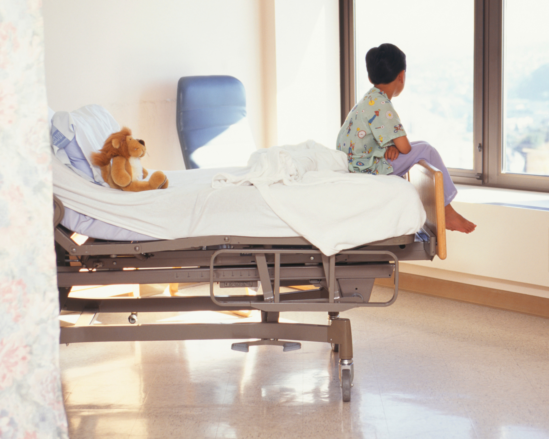 Portrait of a young boy sitting on a hospital bed, looking out the window. Childhood cancer survivorship concept