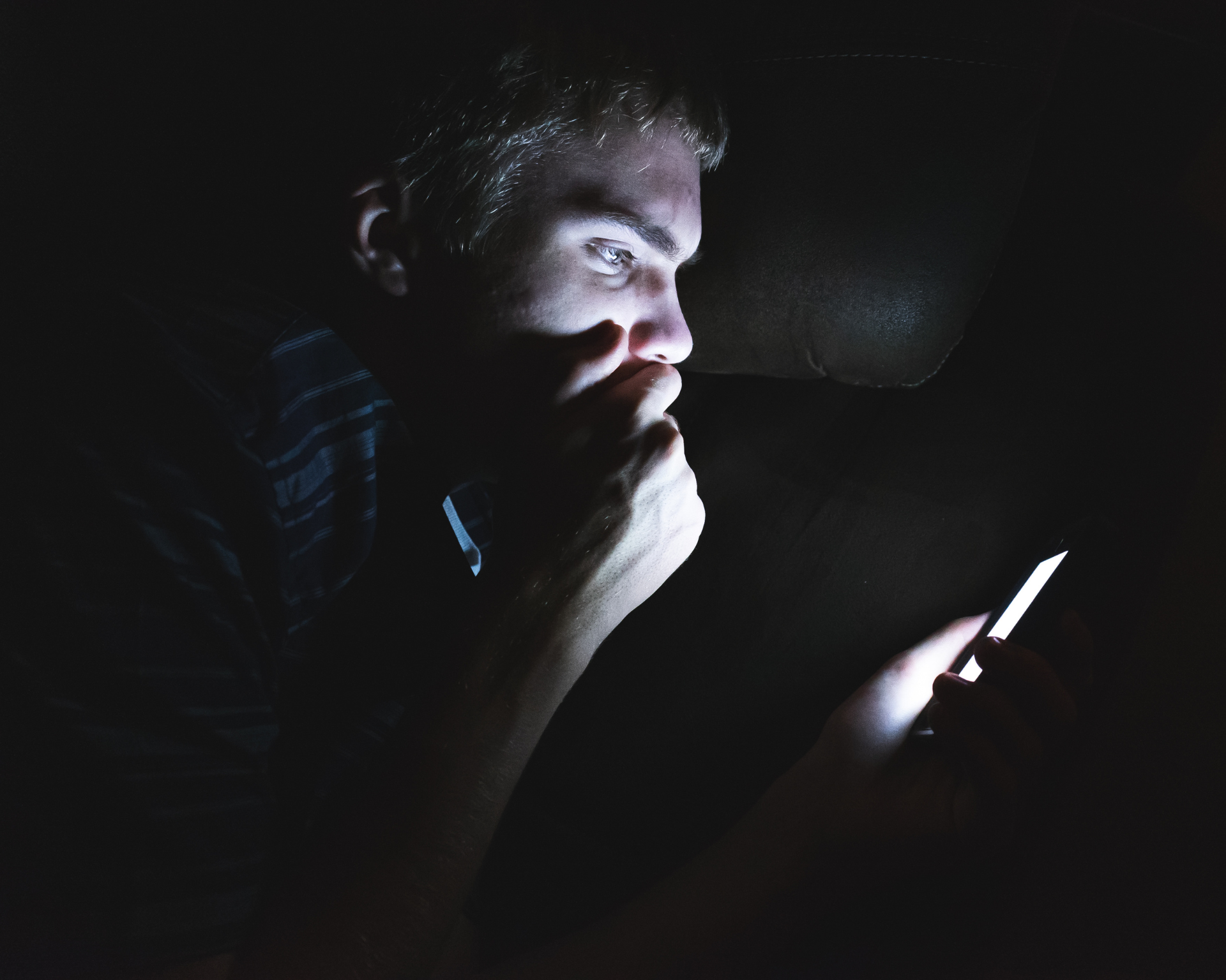 Profile view of a young teenage boy looking at his phone in a dark room