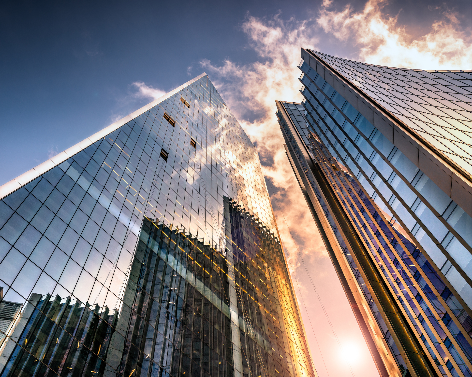 Low-angle view of two tall corporate glass skyscrapers reflecting a blue sky with white clouds. Corporate power concept