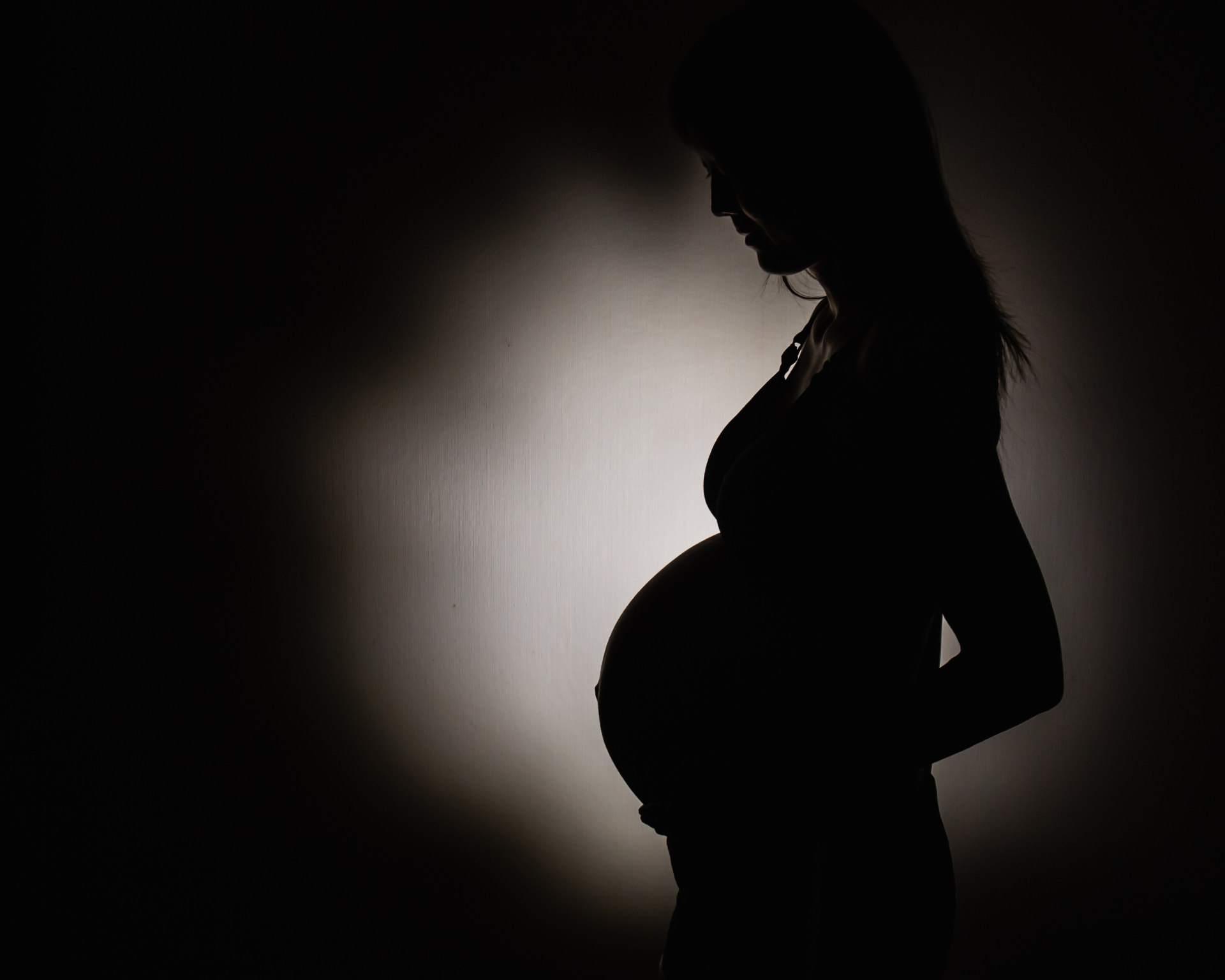 Pregnant woman's shadow with light in the center in room background. Maternal violence concept
