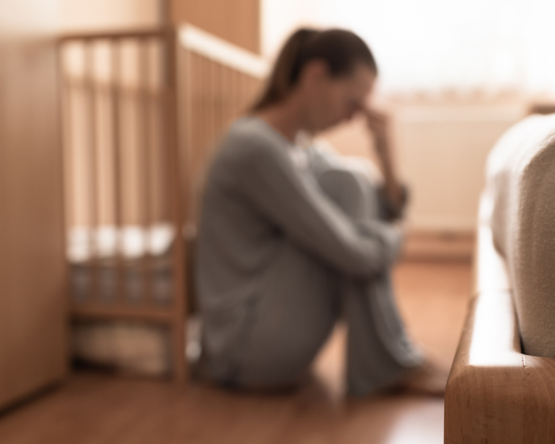 Exhausted new mother leans against baby's crib. Postpartum depression concept