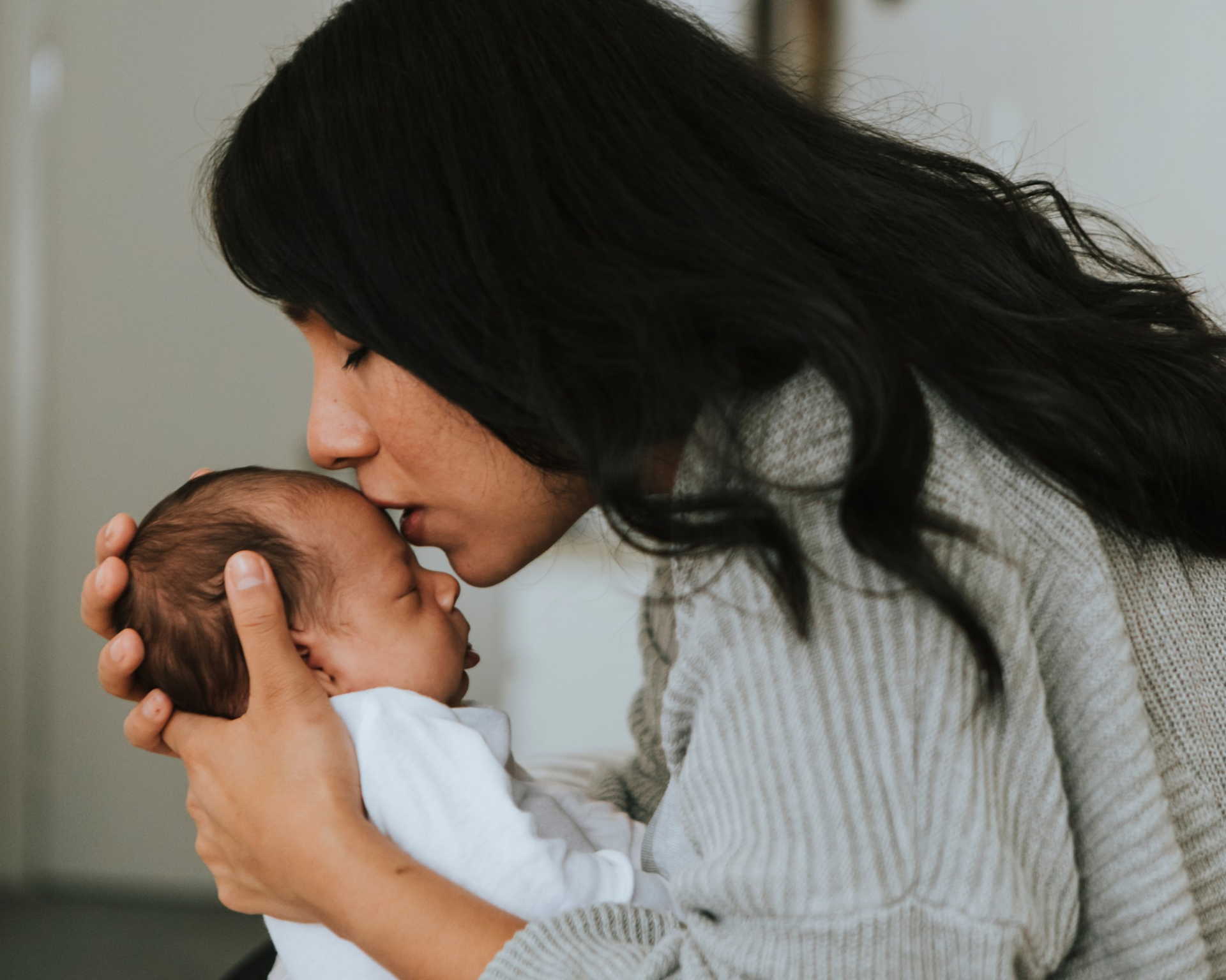 Portrait of a loving mother kissing her infant baby's forehead. Childbirth and post-birth care concept